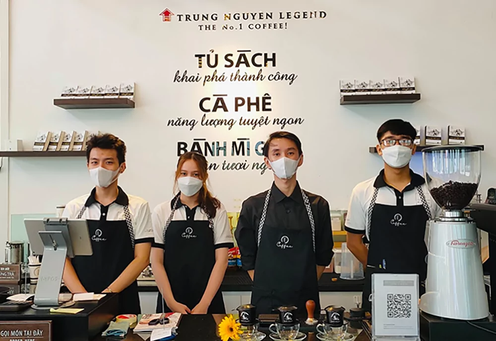 Nhân viên quán cà phê mặc tạp dề đồng bộ, tạo sự chuyên nghiệp.